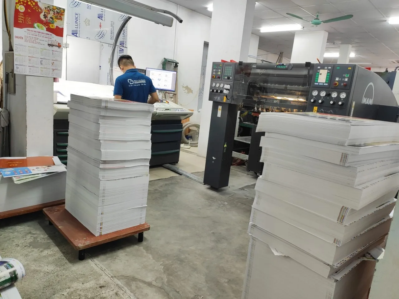 Kỹ thuật viên vận hành máy in và các chồng giấy tại xưởng